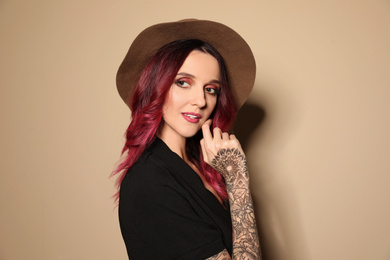 Photo of Beautiful woman with tattoos on arms against beige background