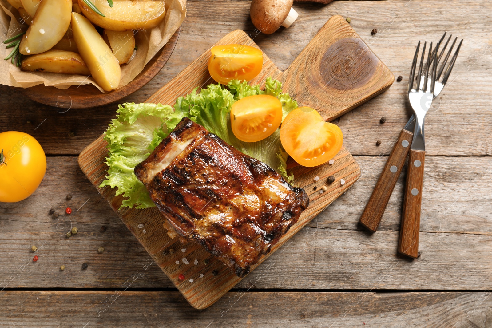 Photo of Board with barbecued ribs and garnish on wooden background, top view