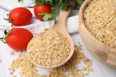 Photo of Spoon with raw bulgur and tomatoes on table, closeup