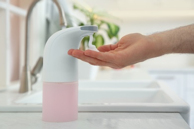 Man using automatic soap dispenser in kitchen, closeup