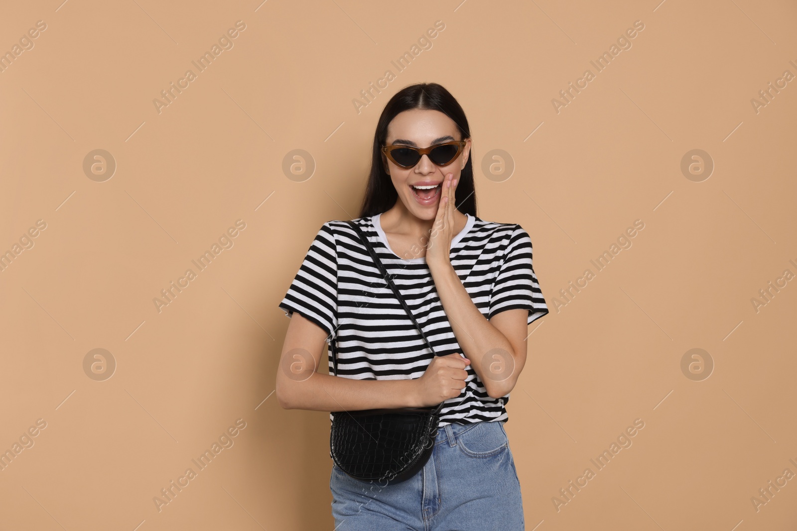 Photo of Beautiful young woman with stylish bag in sunglasses on beige background