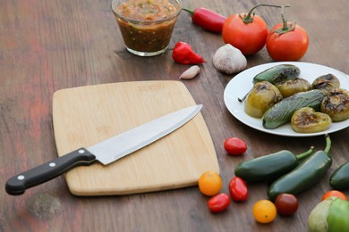 Photo of Salsa sauce, board with knife and ingredients on wooden table