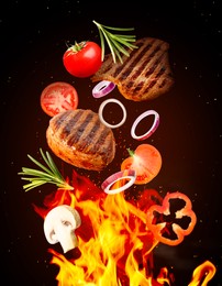 Tasty grilled meat, different vegetables and fire flame on dark background