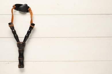 Photo of Black slingshot with pebble on white wooden table, top view. Space for text