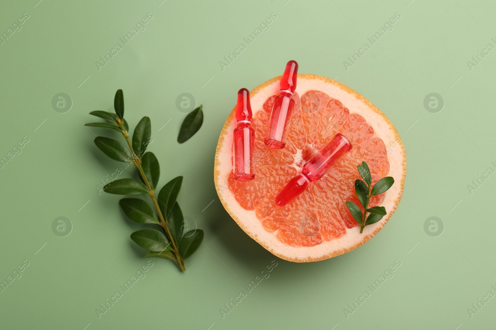 Photo of Skincare ampoules with vitamin C, half of grapefruit and leaves on light green background, flat lay