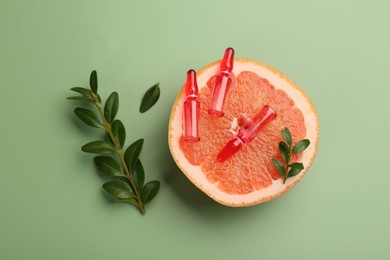 Skincare ampoules with vitamin C, half of grapefruit and leaves on light green background, flat lay