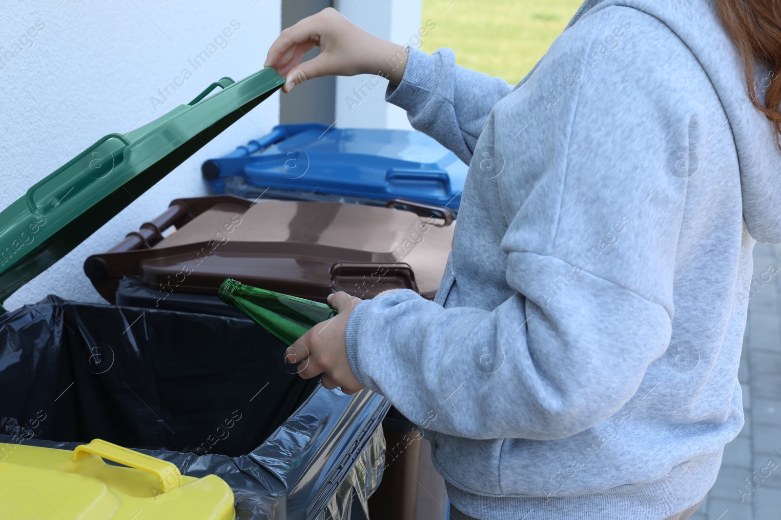 Photo of Woman throwing glass bottle in bin outdoors, closeup. Recycling concept