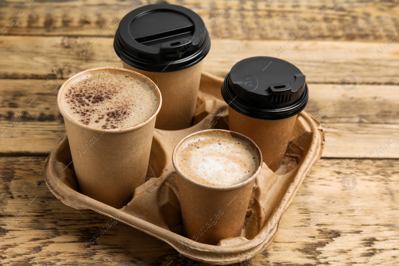 Photo of Takeaway paper coffee cups in cardboard holder on wooden table