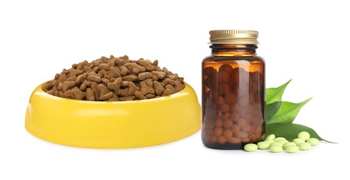 Dry pet food in feeding bowl and bottle with vitamin pills on white background