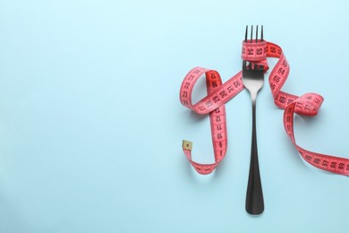 Fork with measuring tape on light blue background, top view and space for text. Diet concept