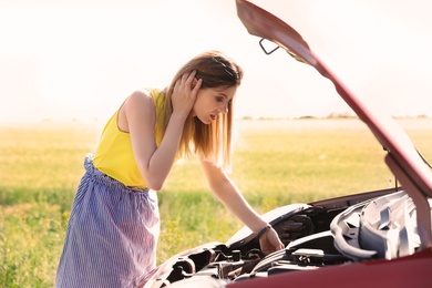 Stressed woman standing near broken car in countryside