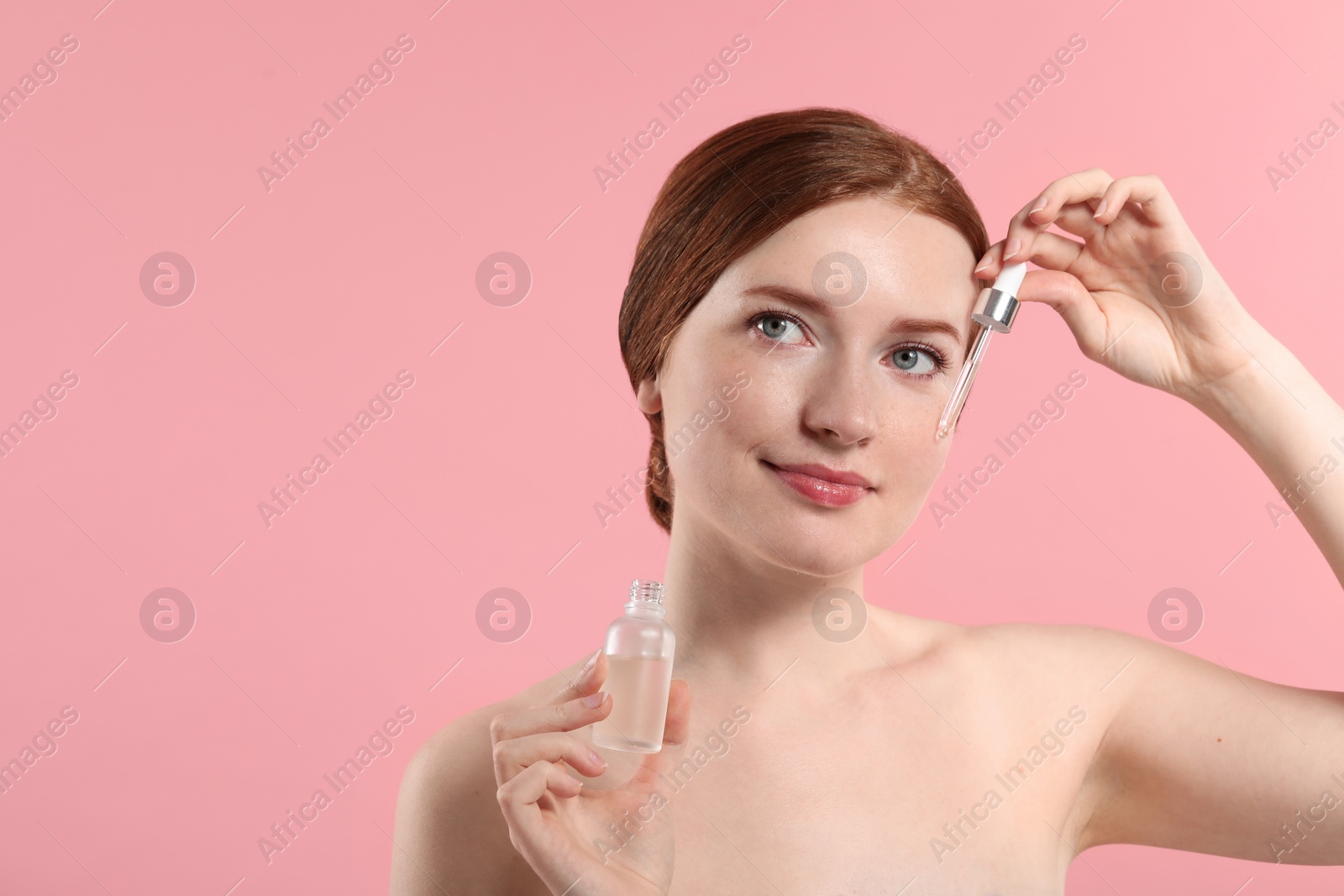 Photo of Beautiful woman with freckles applying cosmetic serum onto her face on pink background. Space for text