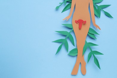 Photo of Woman's health. Female paper figure with uterus and leaves on light blue background, flat lay with space for text