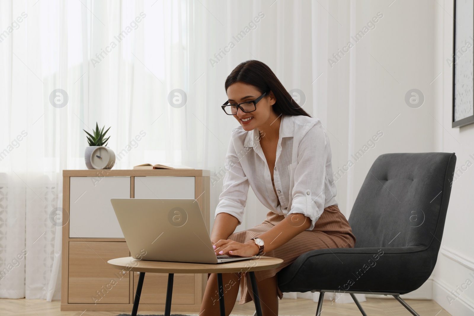 Photo of Young woman using laptop in armchair at home. Internet shopping