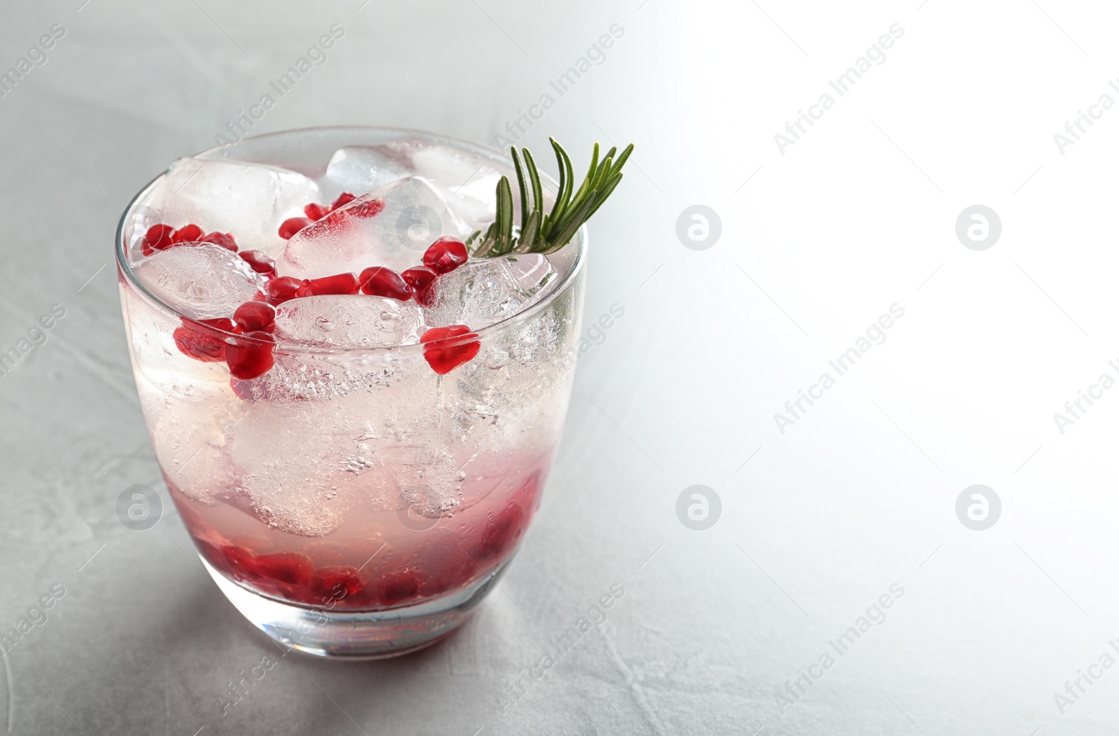 Photo of Tasty cocktail with ice cubes and pomegranate on light grey table, closeup. Space for text