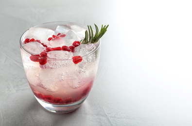 Photo of Tasty cocktail with ice cubes and pomegranate on light grey table, closeup. Space for text
