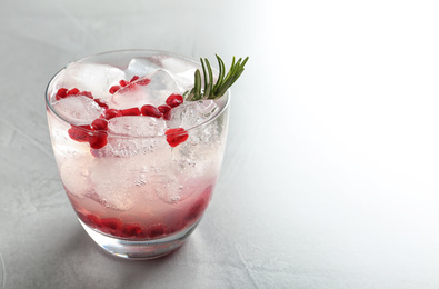 Tasty cocktail with ice cubes and pomegranate on light grey table, closeup. Space for text