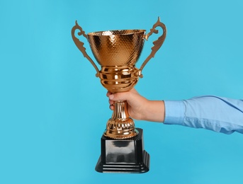 Photo of Boy holding golden winning cup on blue background, closeup