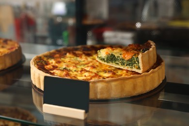 Photo of Delicious quiche with salmon and spinach on counter in bakery shop, closeup. Space for text