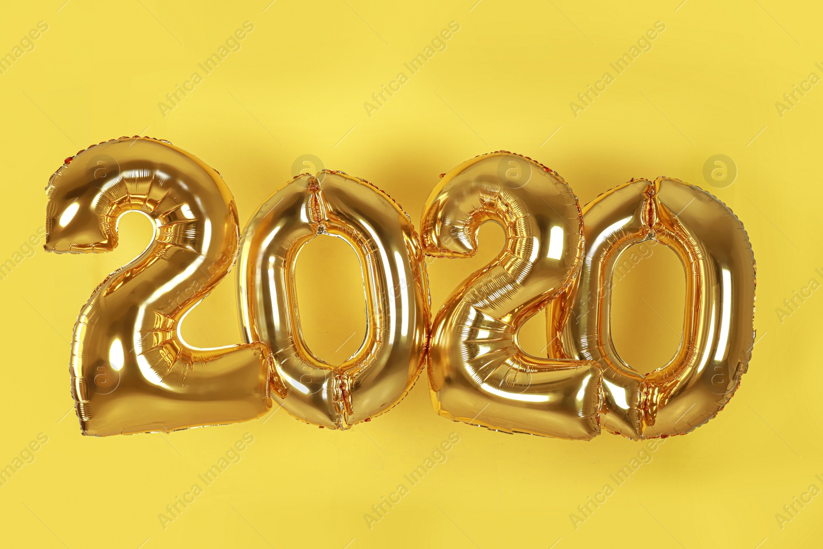 Photo of Golden balloons for party decoration on yellow background. 2020 New Year celebration