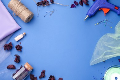 Photo of Hot glue gun and handicraft materials on blue background, flat lay. Space for text