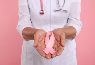 Photo of Doctor with stethoscope holding pink ribbon on color background, closeup. Breast cancer awareness