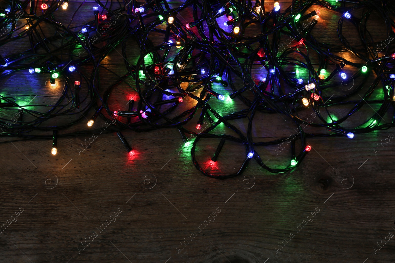 Photo of Colorful Christmas lights on wooden background, top view