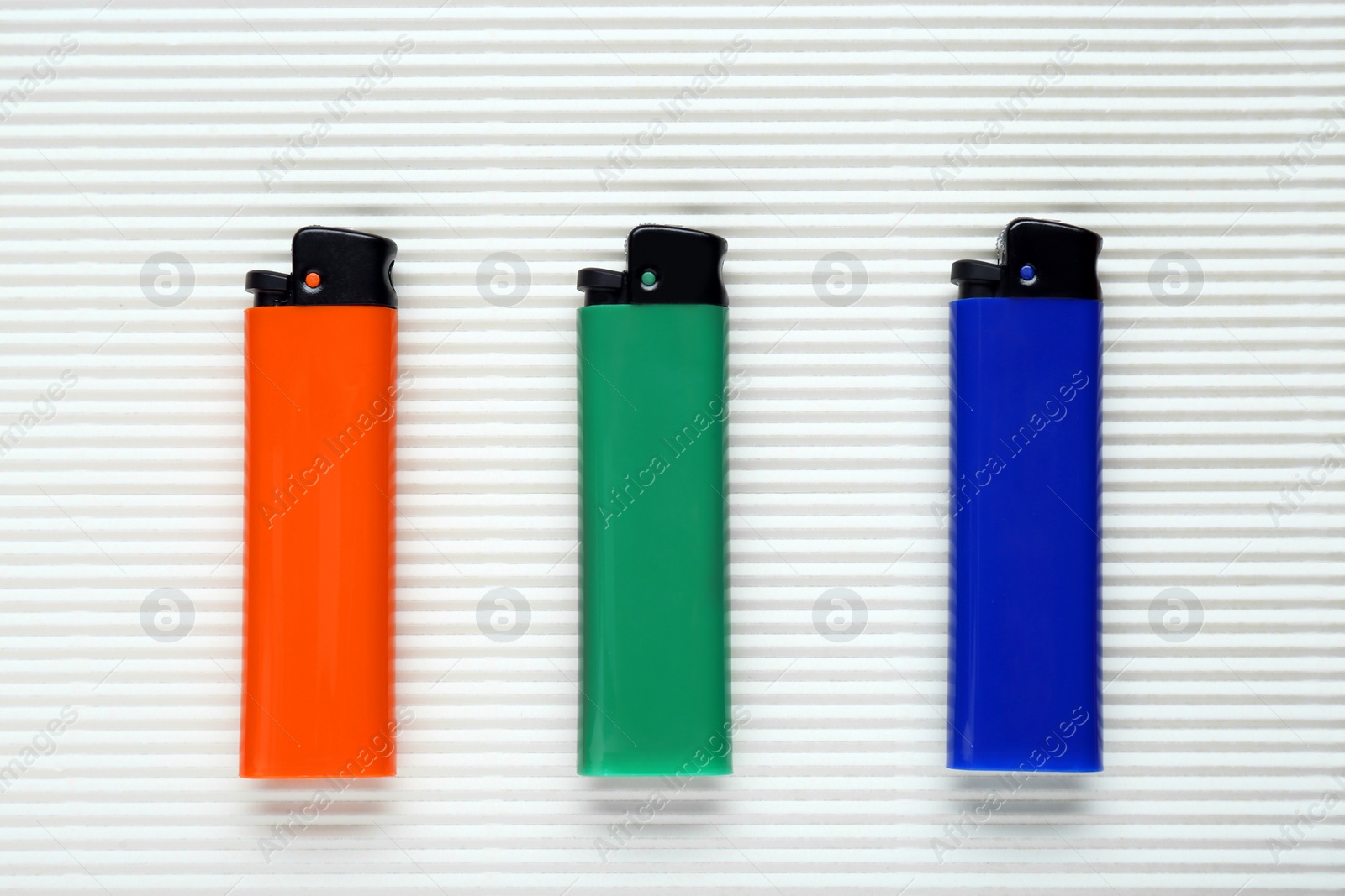 Photo of Stylish small pocket lighters on white corrugated fiberboard, flat lay