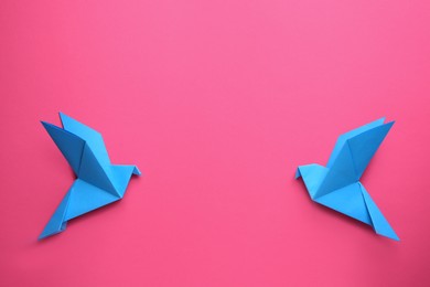 Photo of Beautiful light blue origami birds on pink background, flat lay. Space for text