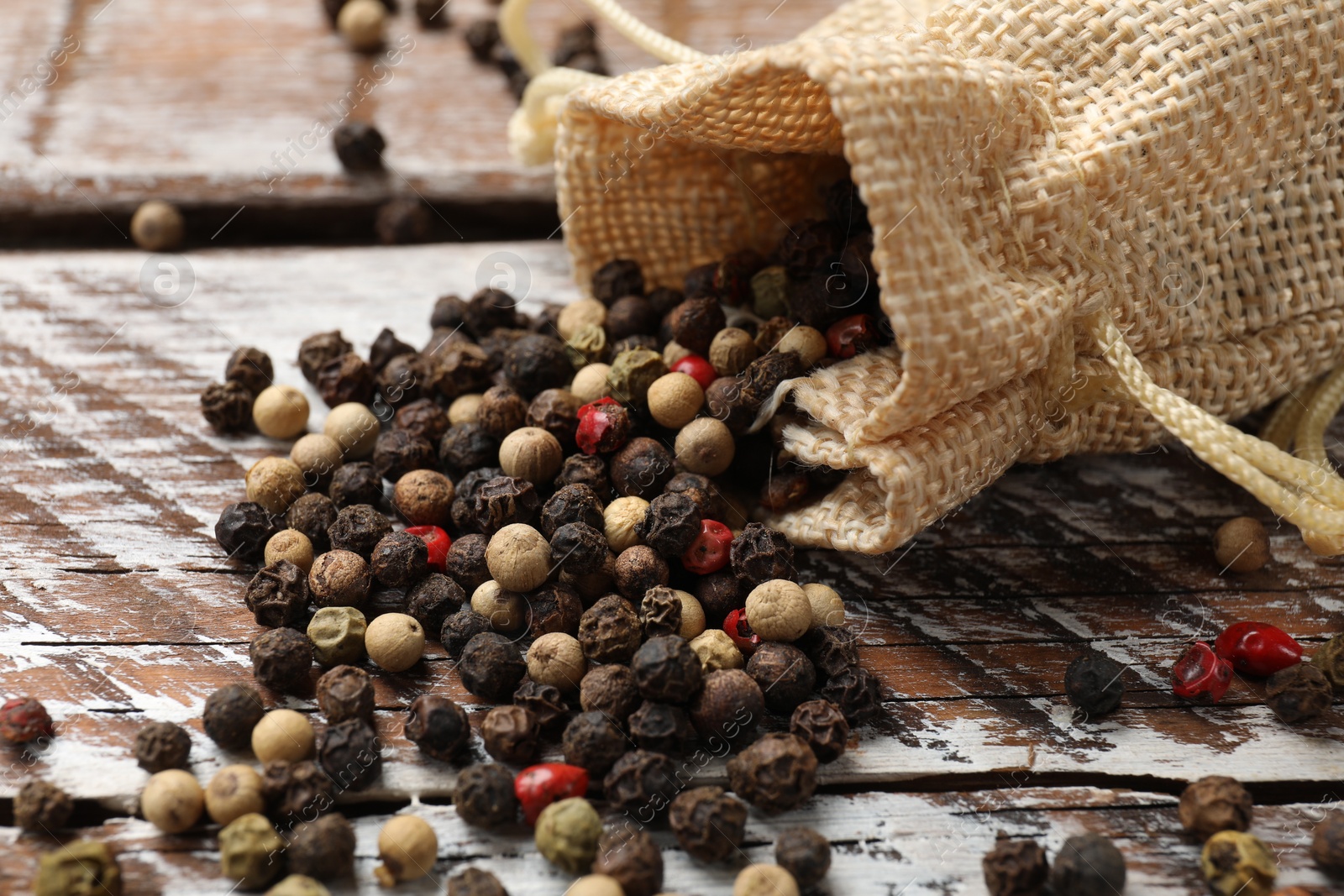 Photo of Aromatic spice. Different peppers in burlap bag on wooden table, closeup