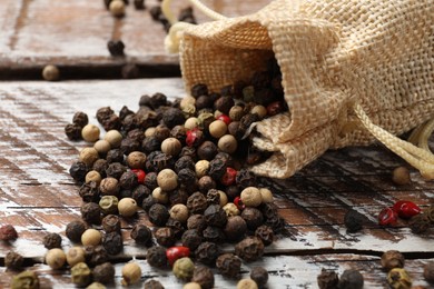 Photo of Aromatic spice. Different peppers in burlap bag on wooden table, closeup