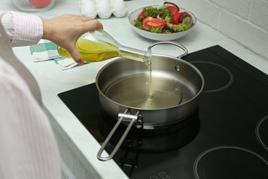 Photo of Woman pouring oil from jug into pan in kitchen, closeup