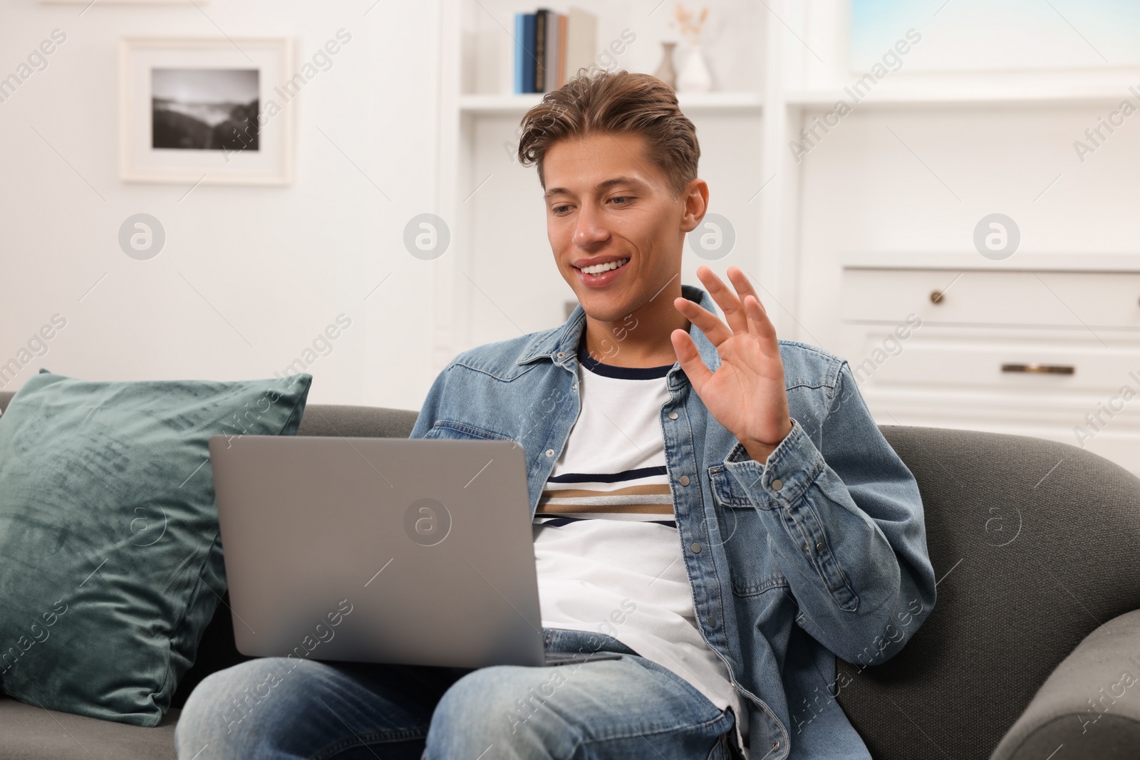 Photo of Happy young man having video chat via laptop on sofa indoors