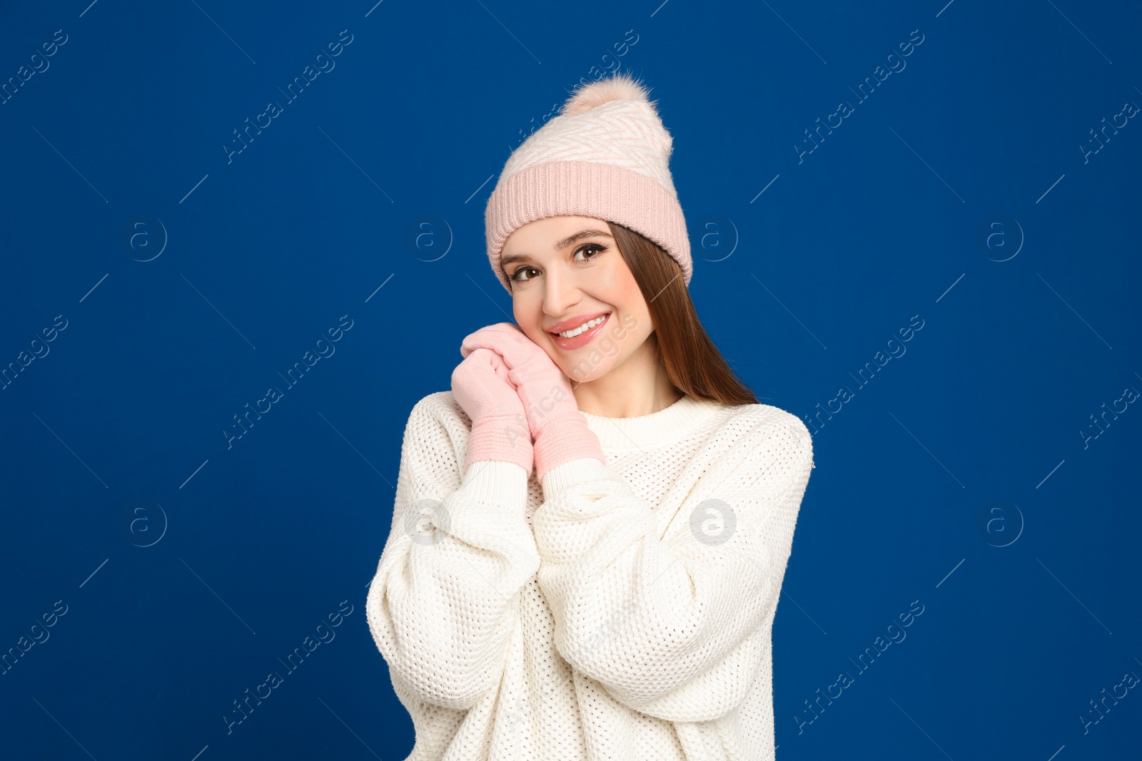 Photo of Young woman wearing warm sweater, gloves and hat on blue background. Winter season