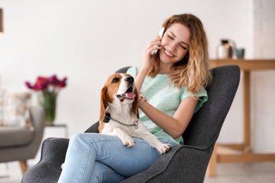 Young woman talking on phone while stroking her dog at home