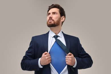 Photo of Confident businessman wearing superhero costume under suit on beige background