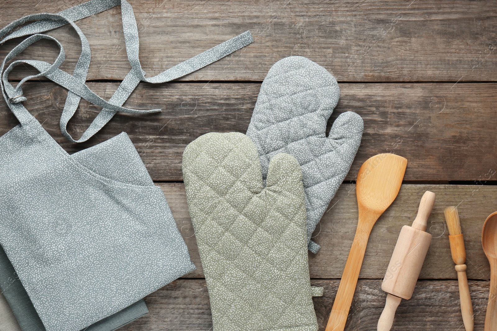 Photo of Kitchen napkin, apron, gloves and different utensils on wooden table, flat lay