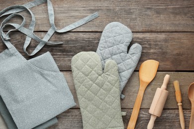 Photo of Kitchen napkin, apron, gloves and different utensils on wooden table, flat lay