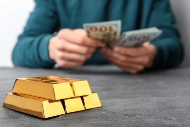 Person counting money at table, focus on stacked gold bars. Space for text
