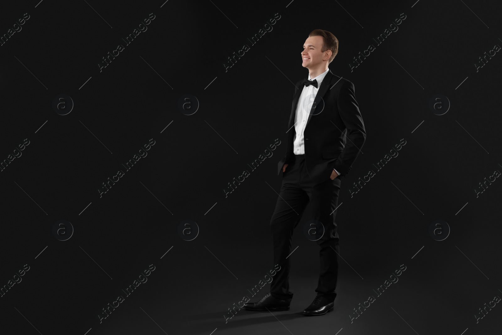 Photo of Handsome young man in stylish suit on black background, space for text