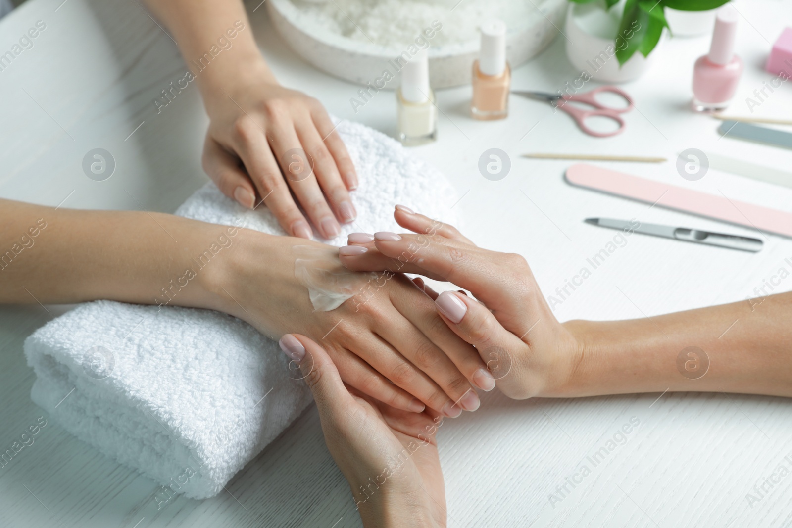 Photo of Cosmetologist applying cream on woman's hand at table in spa salon, closeup