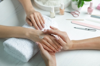 Cosmetologist applying cream on woman's hand at table in spa salon, closeup