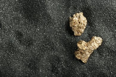 Shiny gold nuggets on black sand, top view. Space for text
