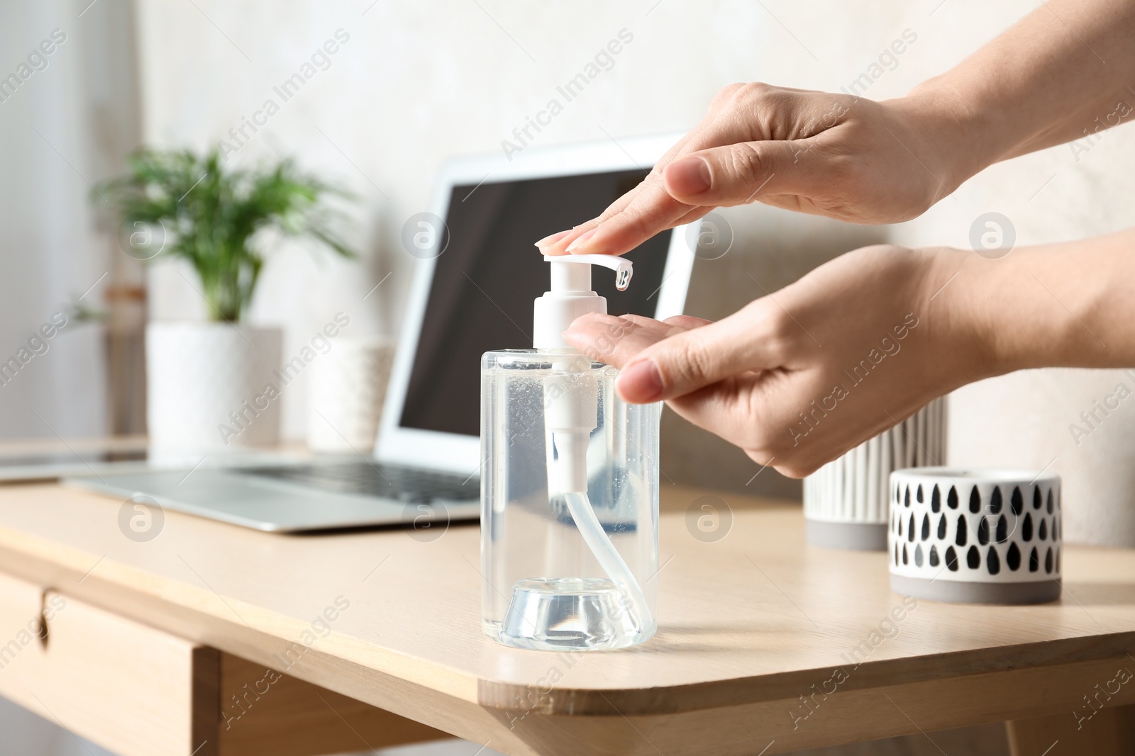 Photo of Woman applying antiseptic gel on hand at workplace, closeup