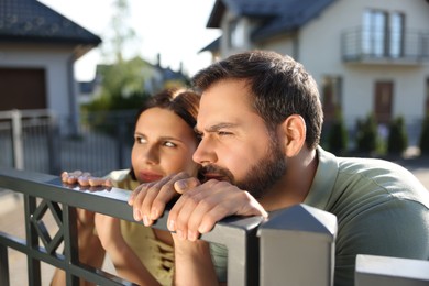 Concept of private life. Curious couple spying on neighbours over fence outdoors