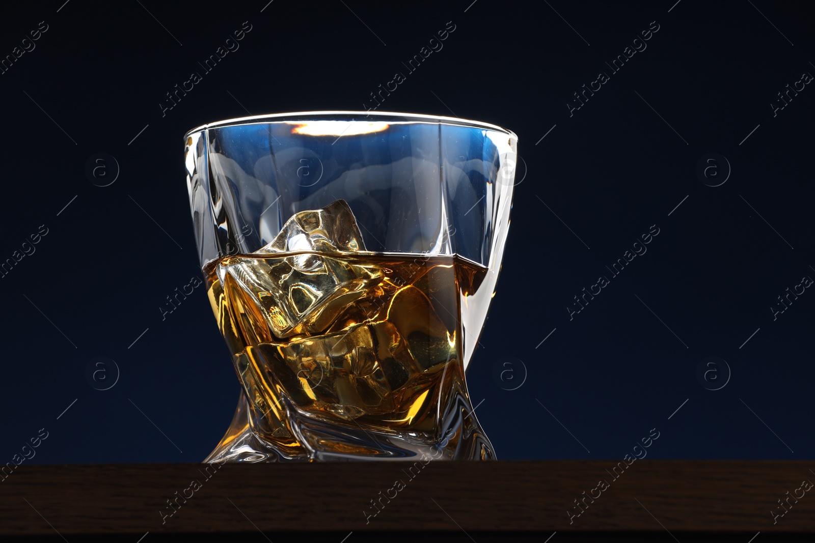 Photo of Whiskey with ice cubes in glass on table against dark blue background