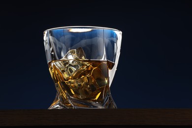 Whiskey with ice cubes in glass on table against dark blue background