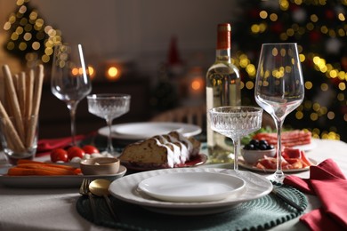 Photo of Christmas table setting with bottle of wine, appetizers and dishware indoors