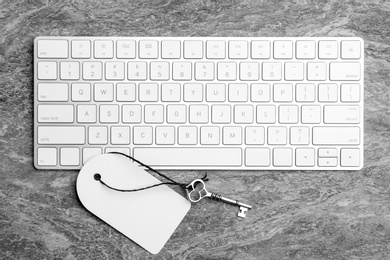 Photo of Key with blank tag and computer keyboard on grey table, flat lay. Keyword concept