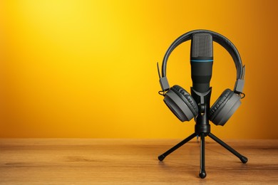 Photo of Microphone and modern headphones on wooden table against orange background, space for text